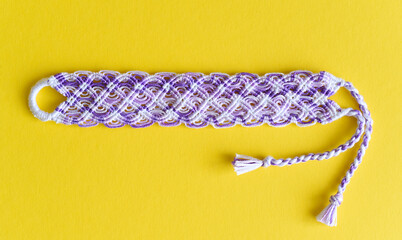 Lilac DIY friendship bracelet with unusual braiding on yellow background