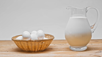 Wicker basket with plenty of eggs near glass jar with fresh milk on wooden table isolated on grey