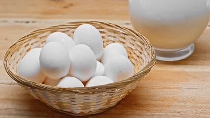 Wicker basket with white eggs near glass jar with fresh milk on wooden surface