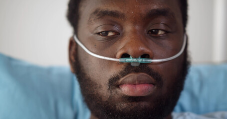 Close up of young african man patient with nasal cannula resting in bed at hospital - obrazy, fototapety, plakaty