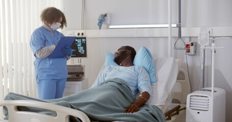 African doctor in safety mask and gloves holding clipboard with test results talking to male patient