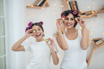 Mom and daughter in hair curlers with pieces of cucumber