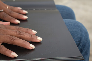 Detail of african american woman´s hands reading braille in a black book.