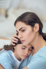 Mom hugging head of teenage daughter with closed eyes