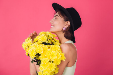 Stylish woman in hat on pink red background hugging large bouquet of yellow asters, spring mood, happy emotions isolated space closed eyes