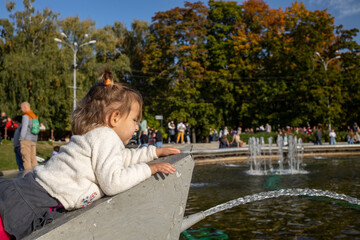 adorable toddler climbs the fountain in the park. weekend walk with children in park in good day