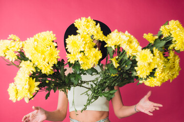 Stylish woman in hat on pink red background throwing to camera large bouquet of yellow asters, spring mood, happy emotions isolated space