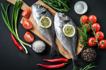 Fresh dorado fish with vegetables and spices on a dark background top view.