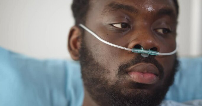 Close up of young african man patient with nasal cannula resting in bed at hospital
