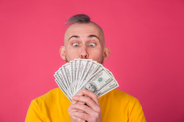 European man on pink red background with fan on 100 dollars shocked excited amazed isolated space