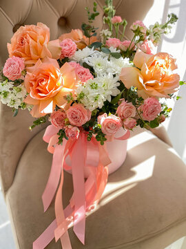 A bouquet of beautiful peach flowers in a box stands on a chair in a flower shop. A composition of roses, white mattiola and chrysanthemum. A gentle gift for a holiday