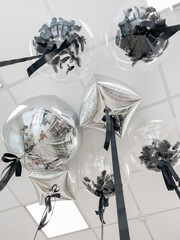 Transparent balloons with black confetti and foil balloons in silver color for a holiday on the ceiling. Stylish design for your birthday