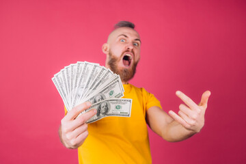 European man on pink red background with fan on 100 dollars with crazy expression rock symbol isolated space