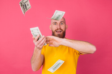 European man on pink red background with fan on 100 dollars happy excited throwing in air isolated space