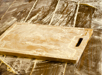 A wooden chopping board with flour and on a dark colored wooden table. suitable as a background theme for floured dishes