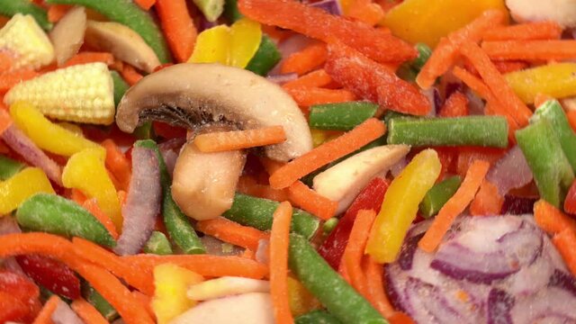 Closeup view 4k stock video footage of mixed frozen icy fresh raw vegetables rotating on white big plate isolated. Organic vegetables background