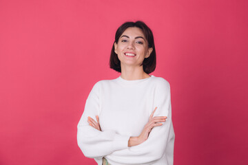 Fototapeta premium Beautiful woman in casual white sweater on pink red background with crossed hands smile look to camera isolated copy space