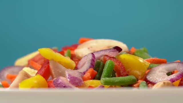 Closeup view 4k stock video footage of mixed frozen vegetables rotating on white big plate isolated on blue background