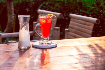 Cold red strawberry drink in a clear glass garnished with yellow lemon peel. Next, a glass of white yogurt is ready to mix up your summer drink. Leave space for the text.