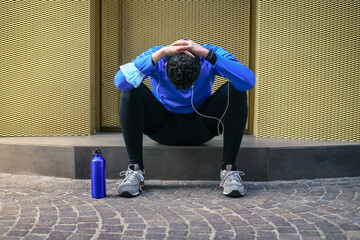 Male doing stretching and listening music after workout. Man resting during city jogging. Runner...