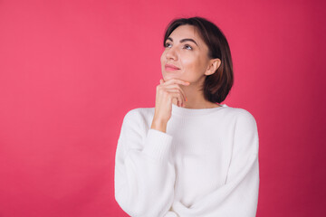 Beautiful woman in casual white sweater on pink red background looks to the side thoughtfully with a sweet smile isolated copy space