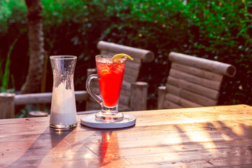 Cold red strawberry drink in a clear glass garnished with yellow lemon peel. Next, a glass of white yogurt is ready to mix up your summer drink. Leave space for the text.