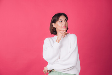 Beautiful woman in casual white sweater on pink red background looks to the side thoughtfully with...