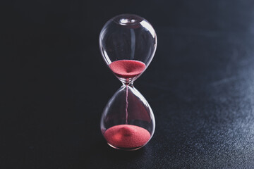 Sand passes through an hourglass, measuring the travel time counting down to the deadline, against...