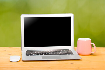 Mockup blank laptop screen with coffee on wooden table in coworking space.