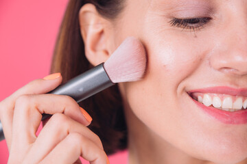 Woman in casual white sweater on pink red background with makeup on face hold blush brush isolated...
