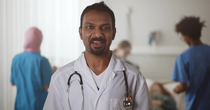Portrait of mature indian doctor looking at camera and talking in hospital ward