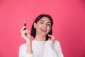 Woman in casual white sweater on pink red background with makeup on face hold blush brush isolated copy space beauty portrait