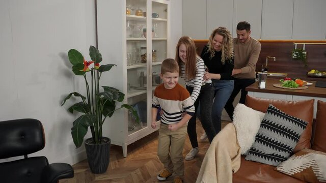 Funny domestic leisure activity of deaf parents and their kids, laughing people dancing in chain holding each other. Cheerful mom, dad, daughter and son with hearing loss playing fool at home