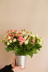 Bouquet of small pink and cream roses in a vase in female hands