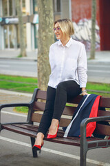 Young funny business woman sitting on a bench after work. Beautiful blond woman with white shirt and red shoes. vertical photo. Freedon. Freelance.