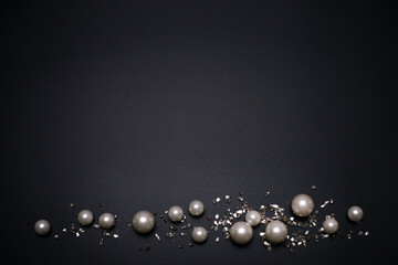 Glitter and pearls on the black background, with free space for text. Top view, elegant flat lay. Beautiful background and template for your design.