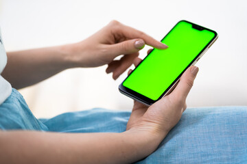 Back view close up of a woman hand using a smart phone with blank screen lying on a couch at home