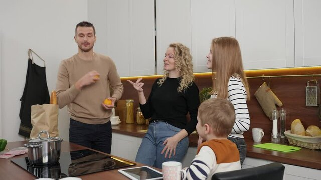 Positive people with hearing disability enjoying domestic leisure, playful father juggling oranges and throwing to children. Happy deaf family using sign language while communicating at home