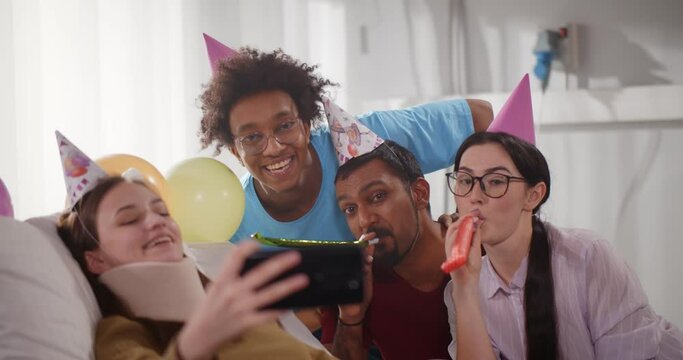 Young injured female with neck brace taking birthday selfie with friends in hospital ward