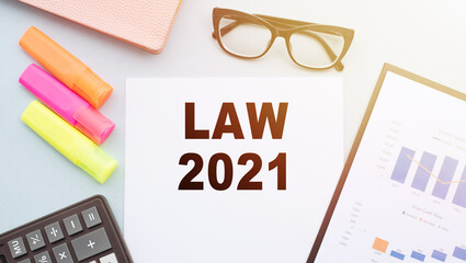 The text LAW 2021 on office desk with calculator, markers, glasses and financial charts.