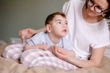 Mother gives a massage to child with cerebral palsy. Rehabilitation therapy at home. Developing...