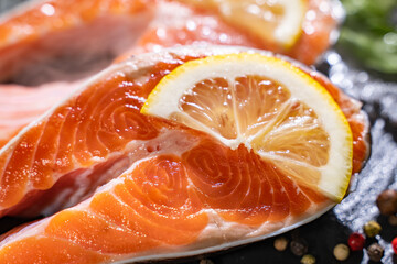Raw salmon fillet on black cutting board with lemon and spices. Healthy food concept. Close up view