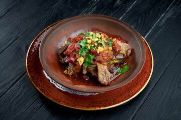 Baked beef with eggplant, nuts, tomatoes and cilantro in clay, served in a bowl on a black background. Restaurant food.