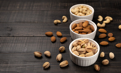 Almonds with cashews and pistachios in white ceramic cups on a dark wooden background. Copy space, no people, flatlay