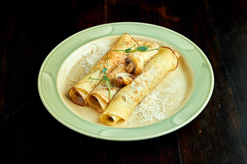 Traditional Ukrainian pancakes with mushroom served in a yellow plate with tomatoes and sour cream on a dark background. Ukrainian Blini with filling