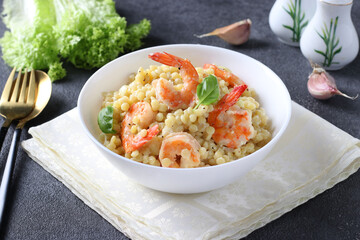Homemade pasta ptitim with shrimps and basil in white plate on gray table. Close-up