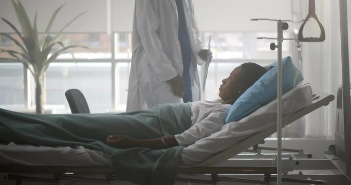African male doctor checking up female patient in hospital ward