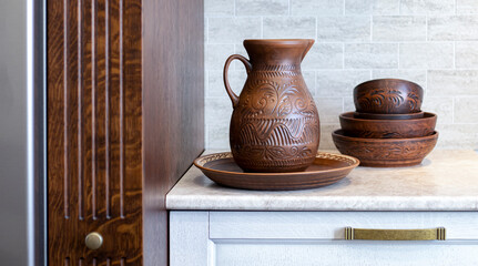 An earthenware jug with a beautiful floral ornament on the background of a wooden kitchen made of solid oak. Pottery, jug, earthenware. 