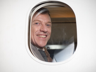 View through the porthole outside the aircraft of passengers. Businessman smiling and looking at the camera on his seat in the airplane at the airport..