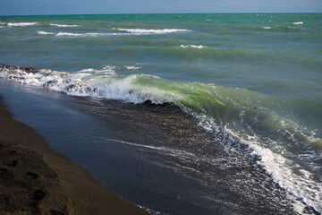 Waves from the ocean seethe and foam on the shore, forming white lambs and foam, close up